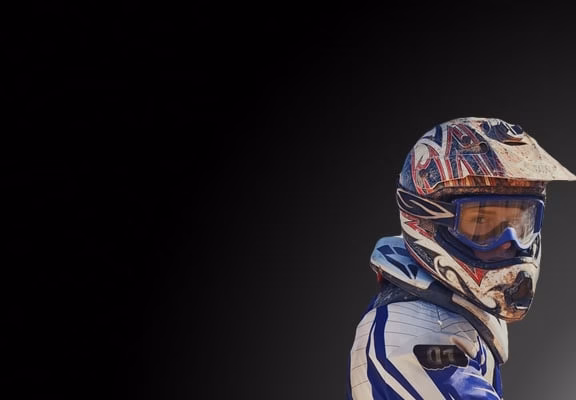 A man in a motorcycle helmet is standing in front of a dark background.