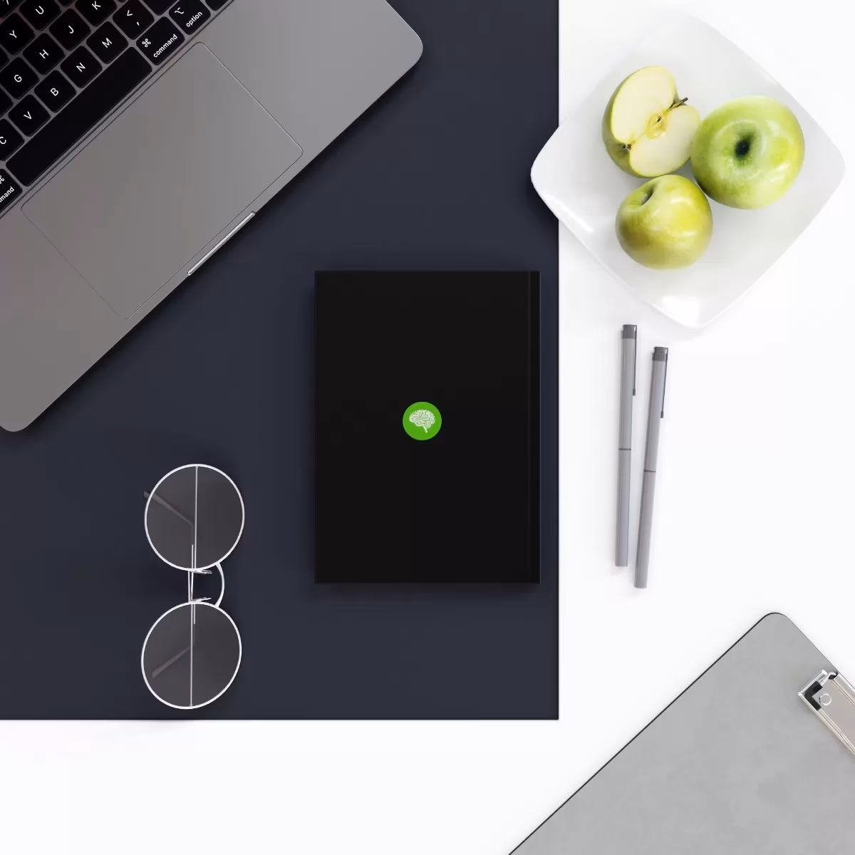A laptop, tablet, phone and Hard Backed Journal on a desk.